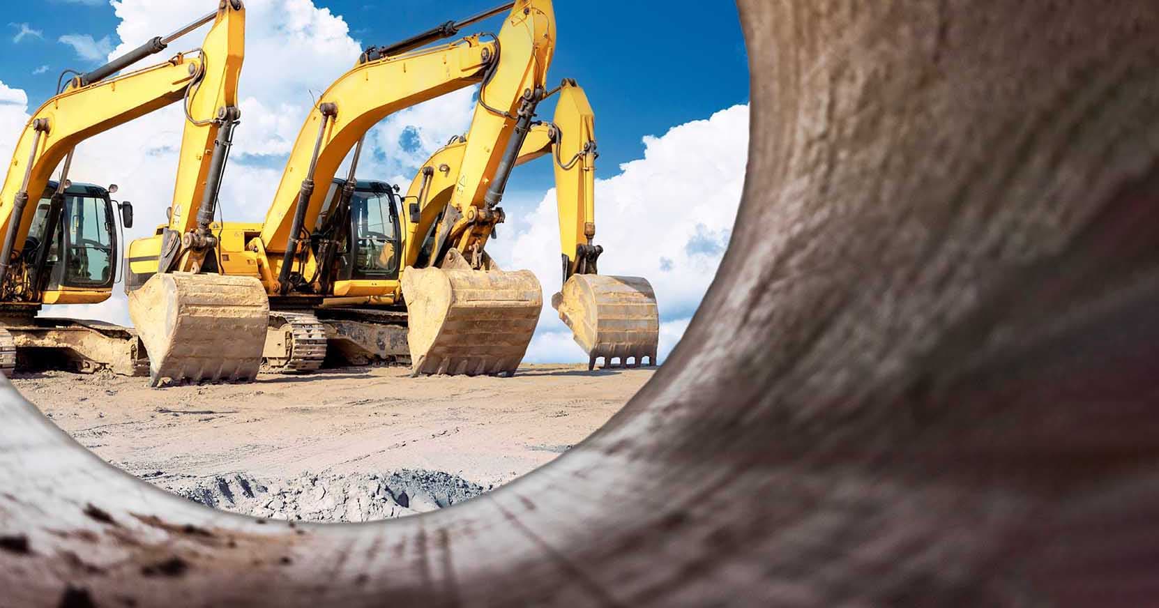 A row of yellow excavators on a work site, seen through the open end of a large pipe