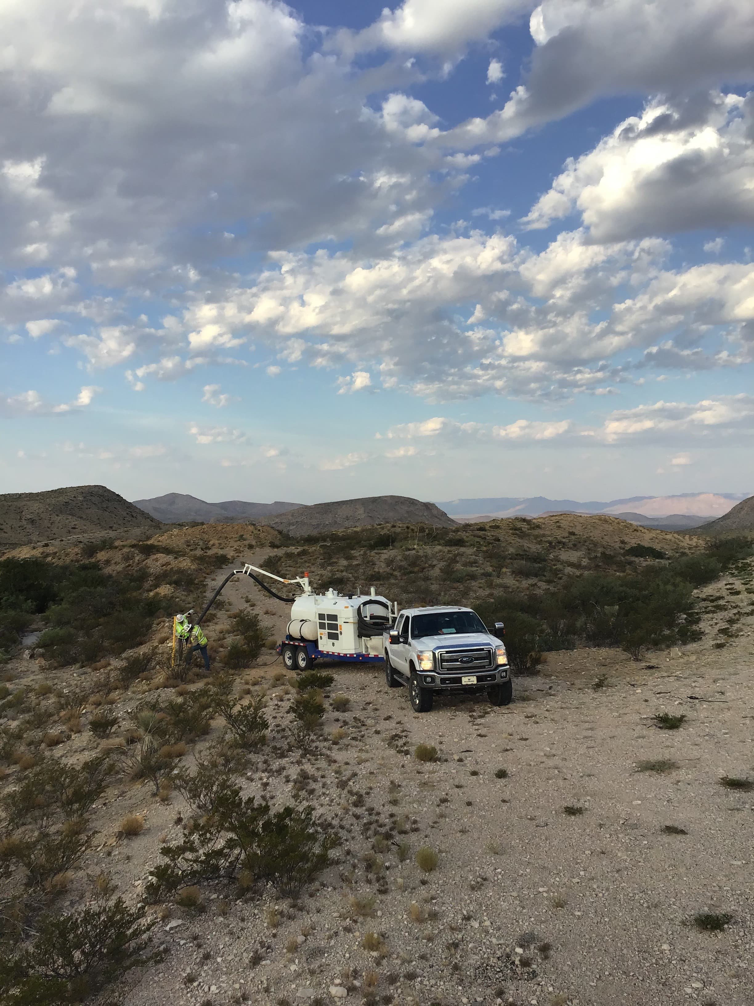A vacuum trailer and pickup truck at a remote desert work site with hills on the horizon