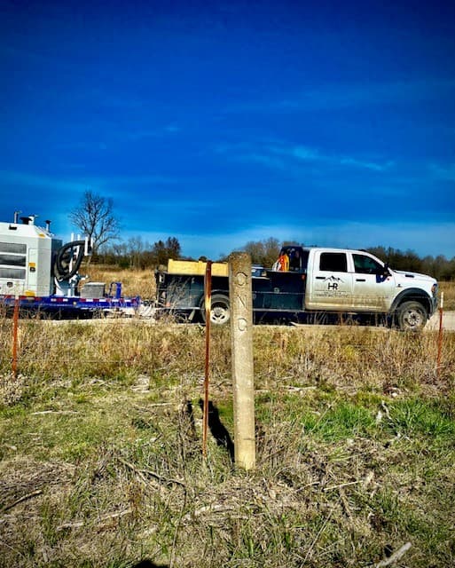 An HR Group service truck and equipment trailer parked beside a marked natural gas pipeline right-of-way